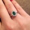 Oval cut emerald claw set with halo of bezel set diamonds on rose gold straight band